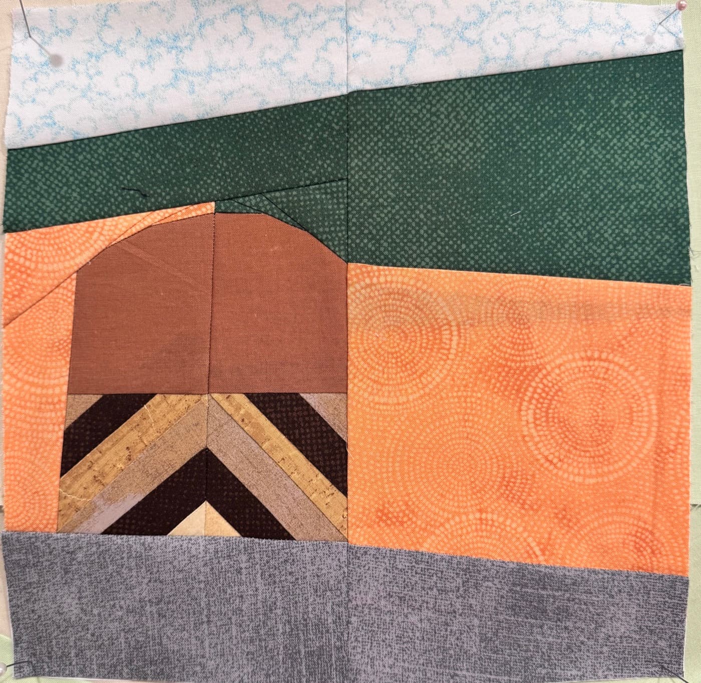 Pieced landscape block with a chevron-patterned building under green hills